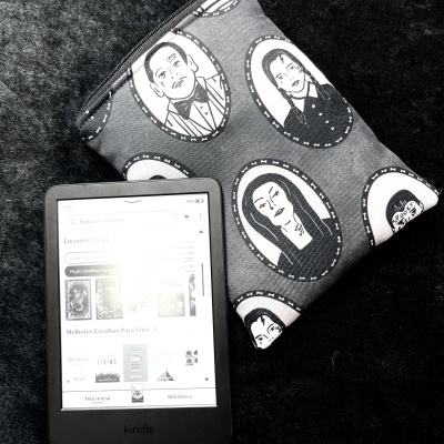Kindle e-reader and gray fabric pouch with black and white gothic portraits on dark surface