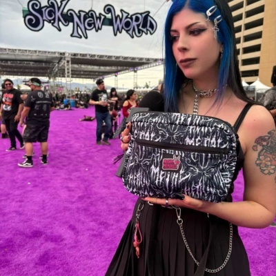 Black and white patterned shoulder bag with MOSHPI MEMORIES patch held by woman with blue hair at event