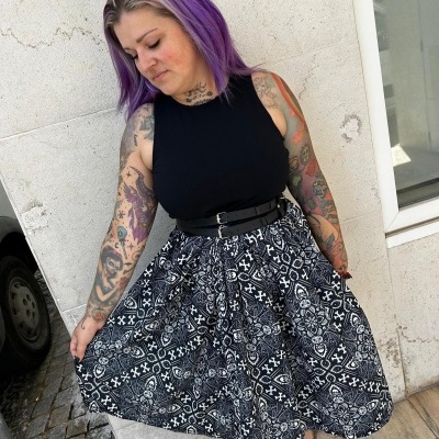 Woman in black sleeveless top and black and white patterned skirt with skull motifs by a stone wall