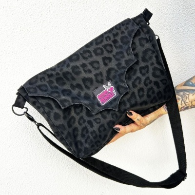 Black leopard print messenger bag with MOSHPIT MEMORIES patch held by tattooed hand