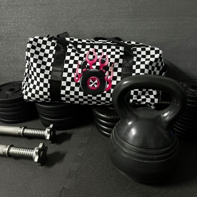 Checkered duffle bag with flaming crossed bones logo among gym weights and kettlebell