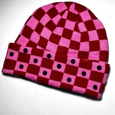Red and pink checkerboard knitted beanie with black buttons on white background.
