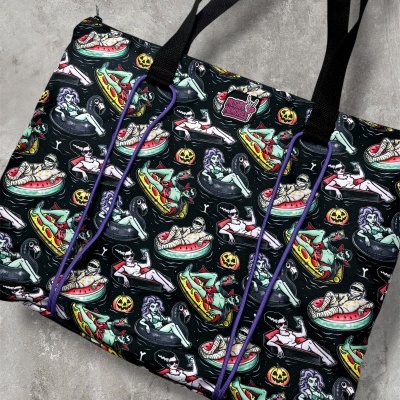 Black tote bag with colorful monster pool float pattern and black handles