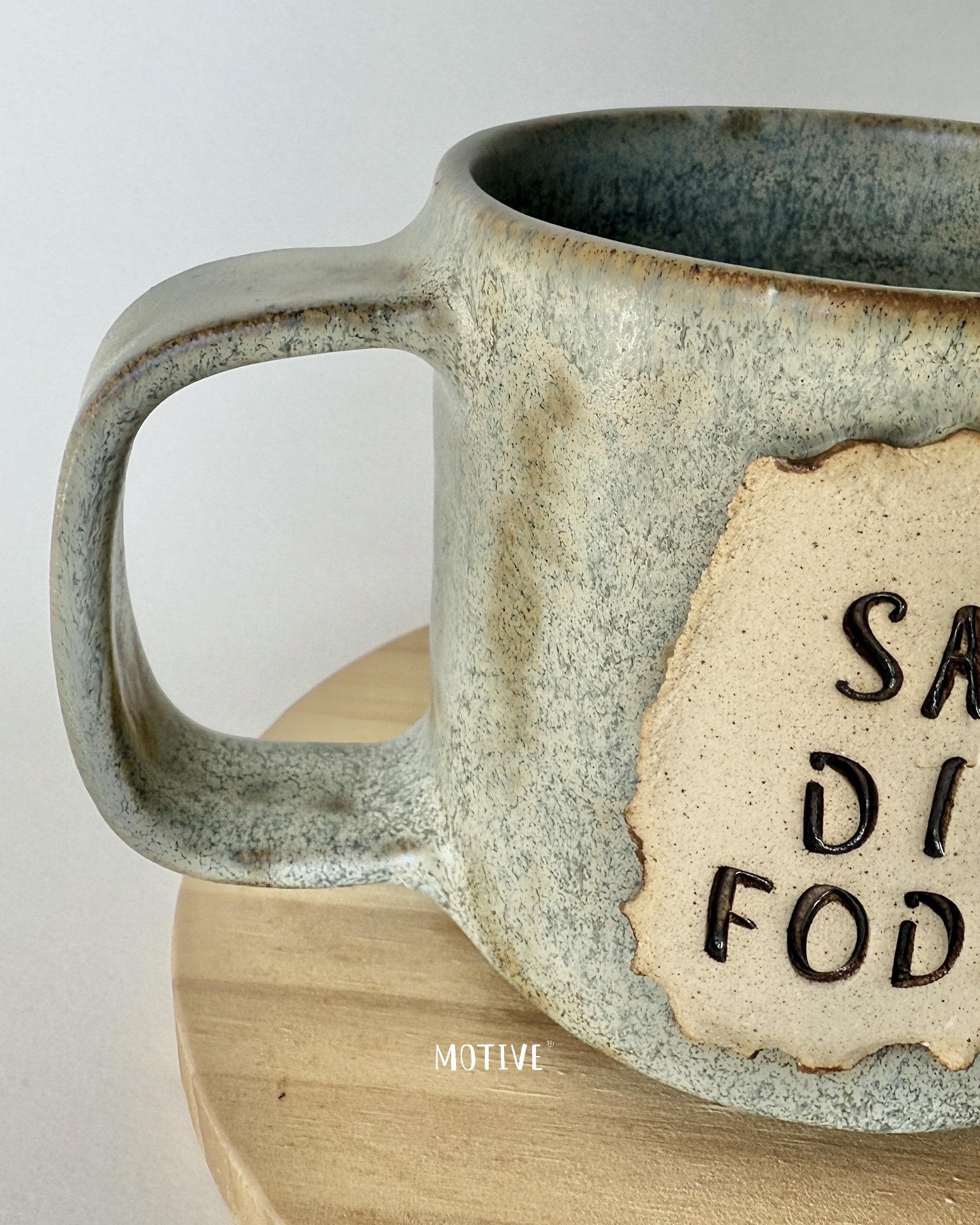 Caneca Sábios Dizem Foda-se Caneca de cerâmica texturizada cinza e bege com alça quadrada e placa de texto em relevo