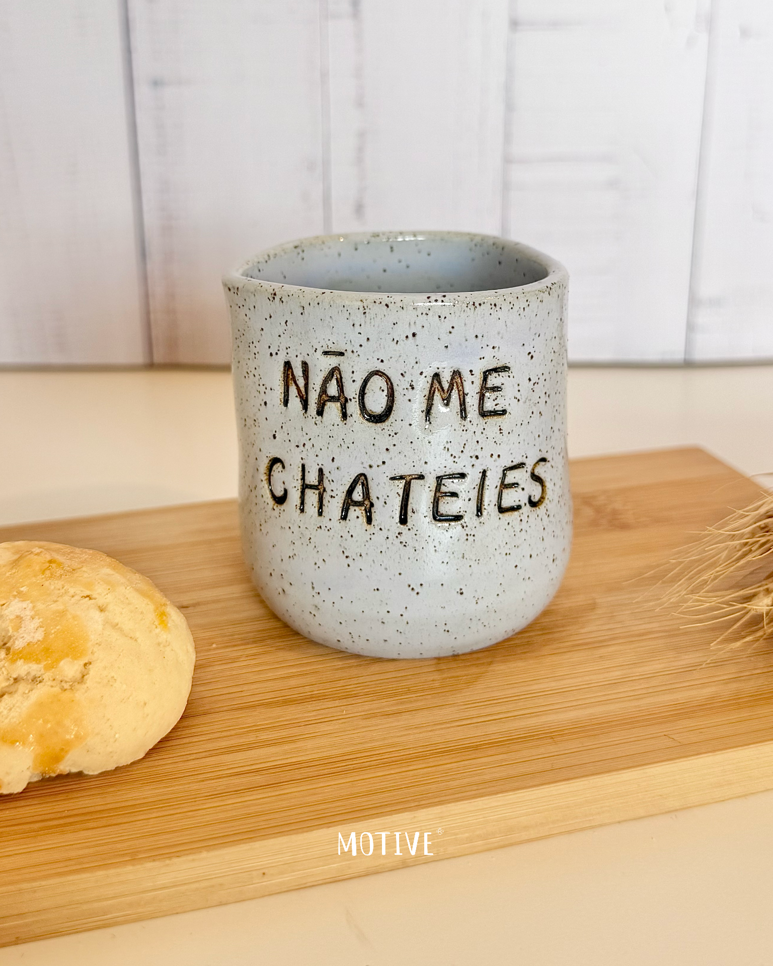 Copinho de Café NÃO ME CHATEIES Caneca cinza claro com texto em relevo NÃO ME CHATEIES sobre tábua de madeira com biscoito ao lado