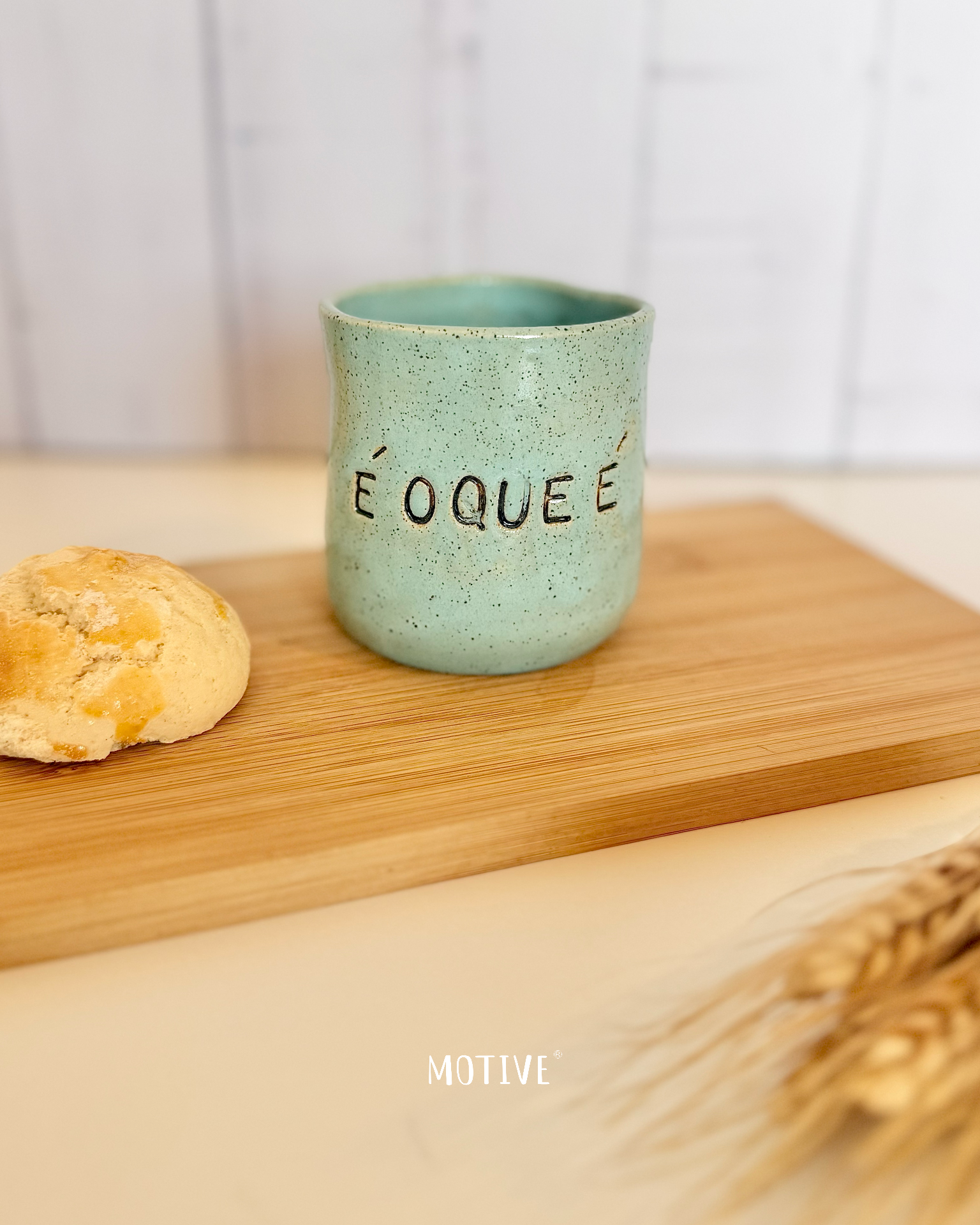 Copinho de Café É O QUE É - Verde menta Caneca cerâmica verde com texto É O QUE É ao lado de pão e espigas de trigo sobre tábua de madeira