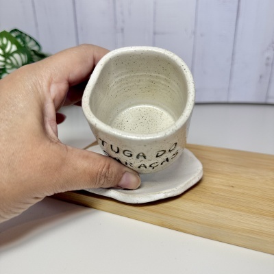 Caneca pequena de cerâmica branca com texto em preto sobre tábua de madeira