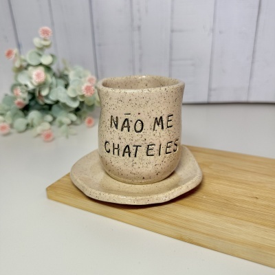 Caneca de cerâmica bege com texto NÃO ME CHATEIES e prato da mesma cerâmica