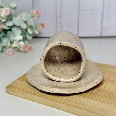 Conjunto de chávena e prato em cerâmica bege com padrão castanho sobre base de madeira e flores ao fundo