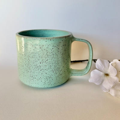 Caneca de cerâmica verde claro com textura salpicada e flores brancas