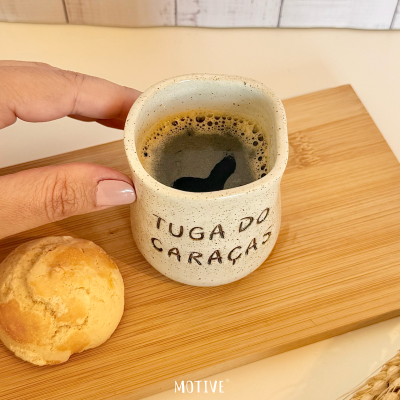 Caneca de cerâmica bege com café sobre base de madeira com pão ao lado