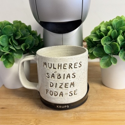 Caneca bege com texto gravado, suporte KRUPS, cafeteira prateada, plantas verdes, madeira clara