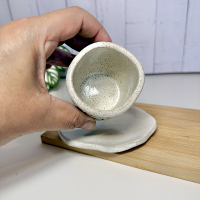 Caneca de cerâmica creme com pires sobre superfície branca e madeira