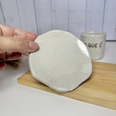 Conjunto cerâmico bege com prato irregular e copo com texto parcial no fundo