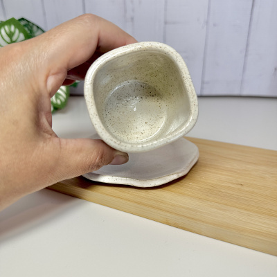 Caneca cerâmica creme com citação gravada e base irregular apoiada numa placa de madeira