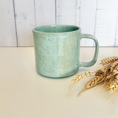 Caneca verde de cerâmica sobre bancada branca com espigas de trigo ao lado
