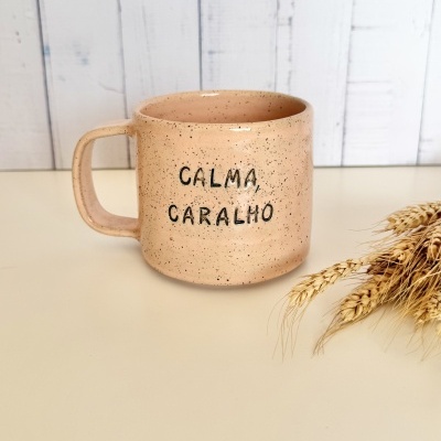 Caneca de cerâmica bege com frase CALMA, CARALHO e ramos de trigo secos