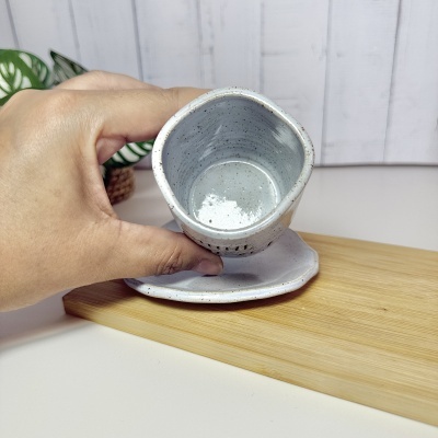 Caneca de cerâmica branca com salpicos castanhos segurada por mão sobre base de madeira