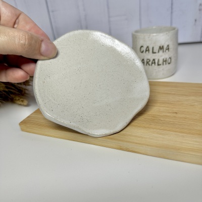 Prato pequeno de cerâmica creme com textura porosa e caneca com texto CALMA CARALHO