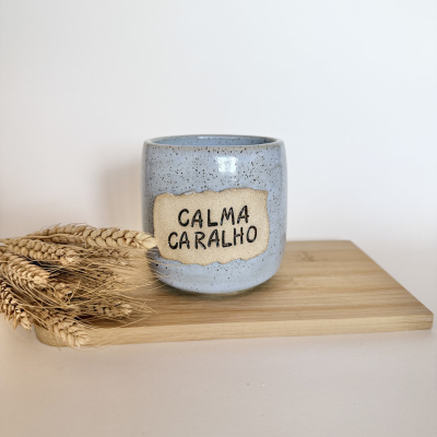 Caneca azul com placa CALMA CARALHO e espigas de trigo em tábua de madeira
