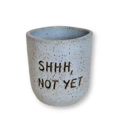 Caneca cilíndrica azul clara de cerâmica com pontos e texto em relevo SHHH, NOT YET.