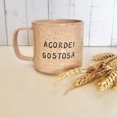 Caneca de cerâmica bege com texto e feixes de trigo ao lado.
