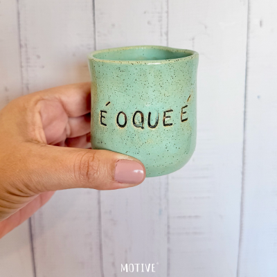 Caneca cerâmica verde clara com a frase É O QUE É na frente