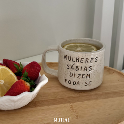 Caneca branca com texto e rodela de limão ao lado de morangos e limão em taça.