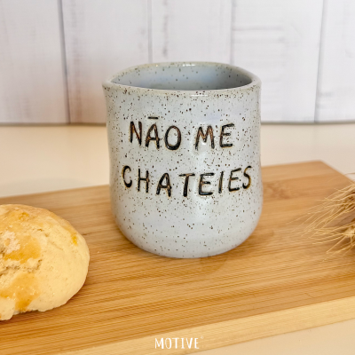 Caneca cinza claro com texto em relevo NÃO ME CHATEIES sobre tábua de madeira com biscoito ao lado