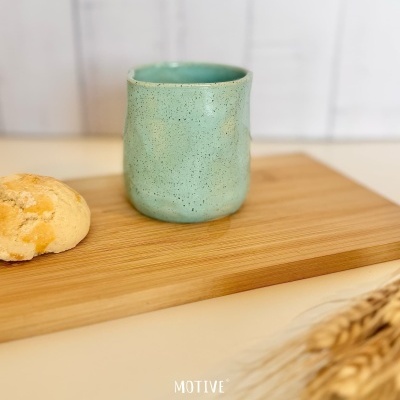 Caneca verde de cerâmica sobre tábua de madeira com pão e trigo ao lado