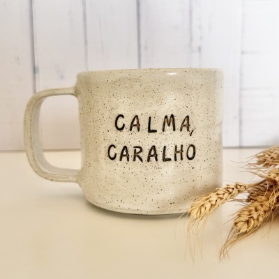 Caneca de cerâmica bege claro com frase CALMA, CARALHO em preto e espigas de trigo ao lado