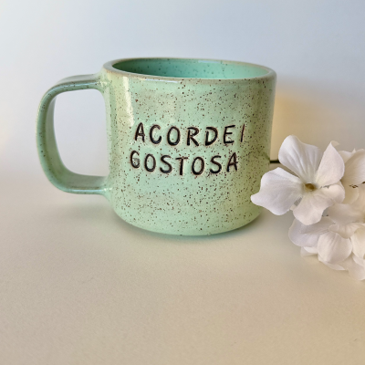Caneca verde com texto em relevo e flores brancas ao lado