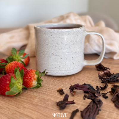 Caneca de cerâmica bege com chá e morangos frescos em madeira clara