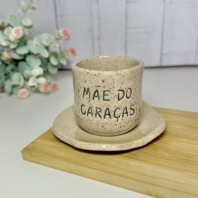 Chávena e prato de cerâmica bege com pontilhado e texto em preto numa tábua de madeira