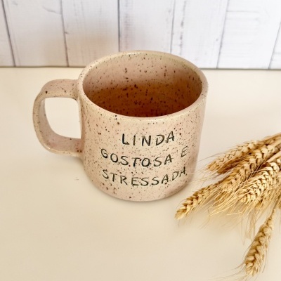 Caneca de cerâmica creme com texto preto e espigas de trigo secas ao lado.