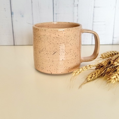 Caneca de cerâmica bege com manchas pretas e espigas de trigo secas.