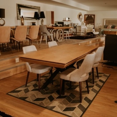 Mesa de madeira com seis cadeiras estofadas em tecido bege claro e tapete geométrico em sala de exposição