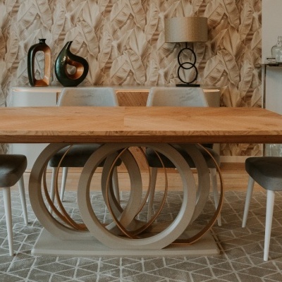 Mesa de madeira clara com base circular decorativa e cadeiras cinzentas numa sala moderna