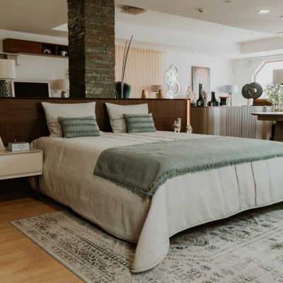 Quarto moderno com cama de madeira, colcha bege, manta cinza esverdeada e tapete claro