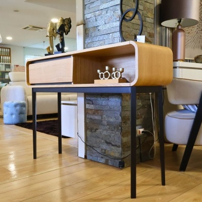 Mesa de apoio de madeira clara e pernas pretas num ambiente interior com decorações e mobiliário moderno.