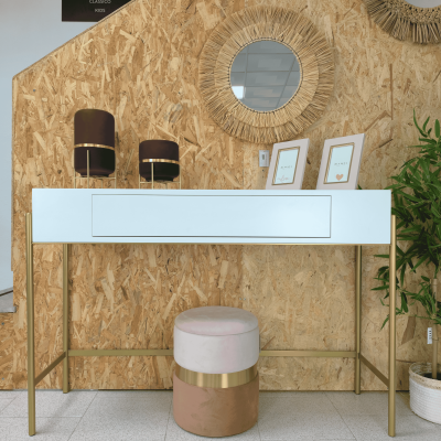 Mesa de apoio branca com lâmpadas castanhas, quadros pequenos brancos, espelho redondo de fibras e pufe bege e rosa