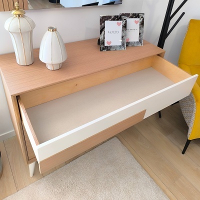 Móvel com gaveta aberta, vasos brancos dourados e molduras de fotos em cima