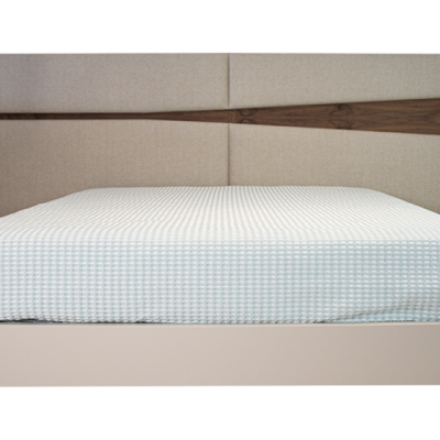 Cama com cabeceira estofada bege e detalhe em madeira, colchão azul claro quadriculado.