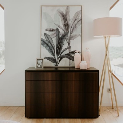 Cómoda de madeira escura com decoração e luminária de chão em ambiente claro com janelas hexagonais