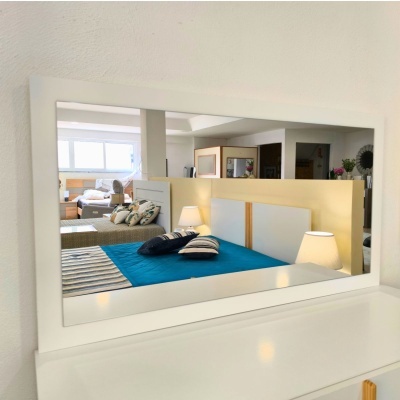 Espelho branco refletindo um quarto com cama, almofadas e luminária