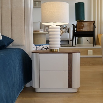 Mesa de cabeceira com candeeiro branco ao lado de cama com colcha azul escura