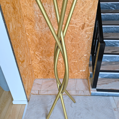 suporte metal dourado com hastes entrelaçadas em interior com carpete, parede de madeira, escada