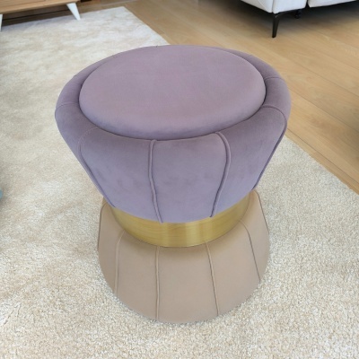 Pufe redondo lilás com base dourada sobre tapete claro num interior