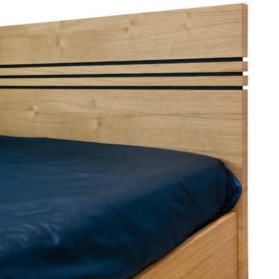 Cama de madeira clara com lençol azul escuro e detalhes pretos na cabeceira