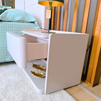 Mesa de cabeceira branca com gaveta aberta e candeeiro em quarto com cama azul clara